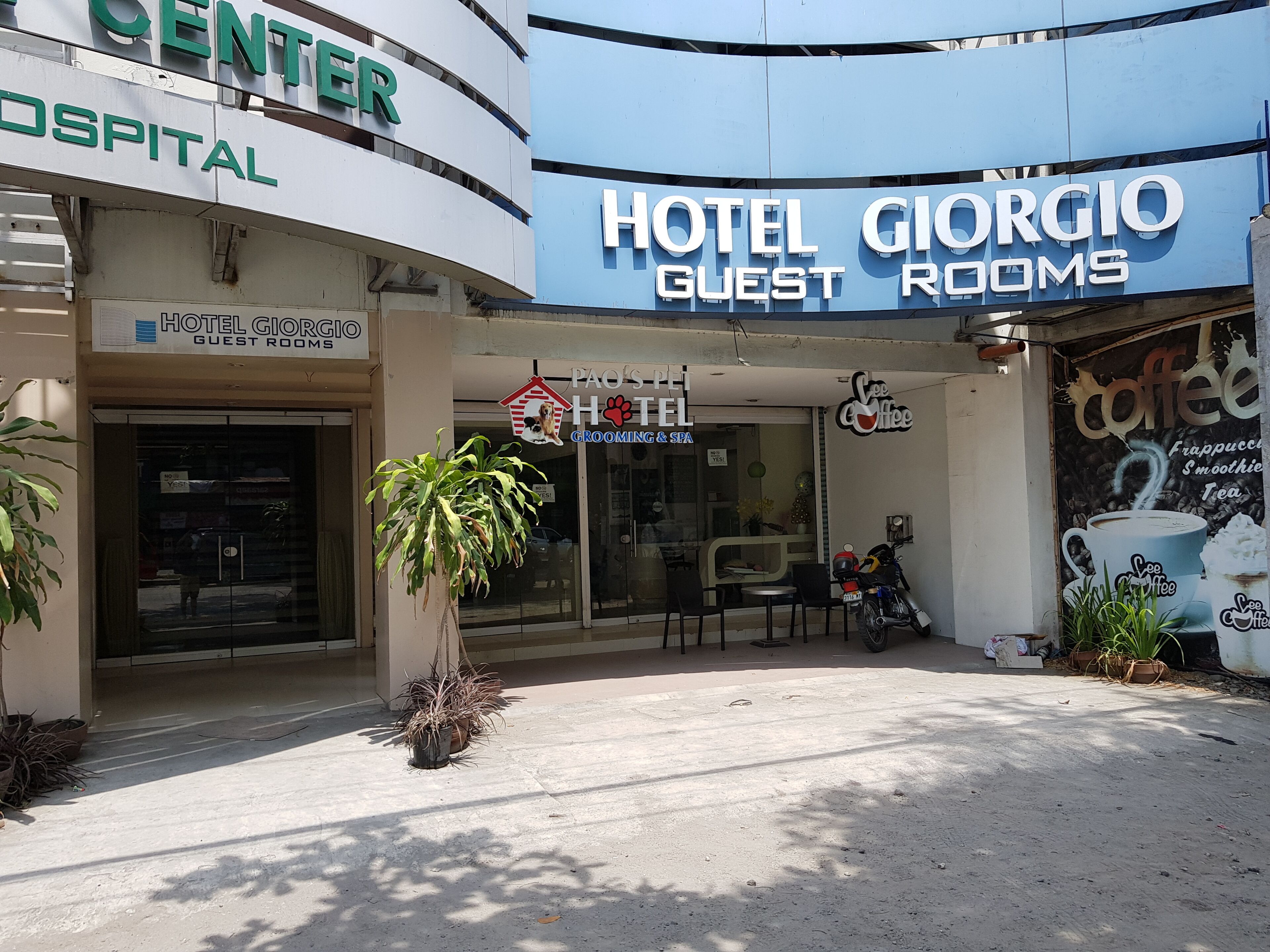 Um hotel chamado 'Hotel Giorgio Guest Rooms' com um letreiro de 'Paos-Pi Hotel Grooming & Spa' e uma cafeteria chamada 'See Coffee'.