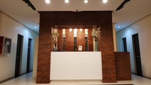 Un área de recepción con un mostrador de madera, dos plantas en macetas y un cartel sobre el mostrador.