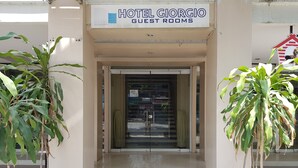 La entrada a Hotel Giorgio Guest Rooms, con una puerta de cristal transparente, plantas en macetas a ambos lados y un letrero sobre la puerta.