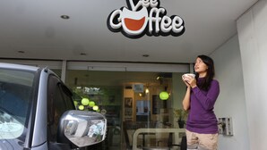 Una persona parada frente a una cafetería, con un letrero que dice 'Lee Coffee'.