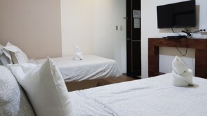 Habitación de hotel con dos camas, un televisor de pantalla plana montado en un estante de madera y una puerta con un cartel de ahorro energético.