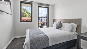 Quarto de hotel moderno com uma cama grande, uma escrivaninha e vista para a cidade pelas janelas.