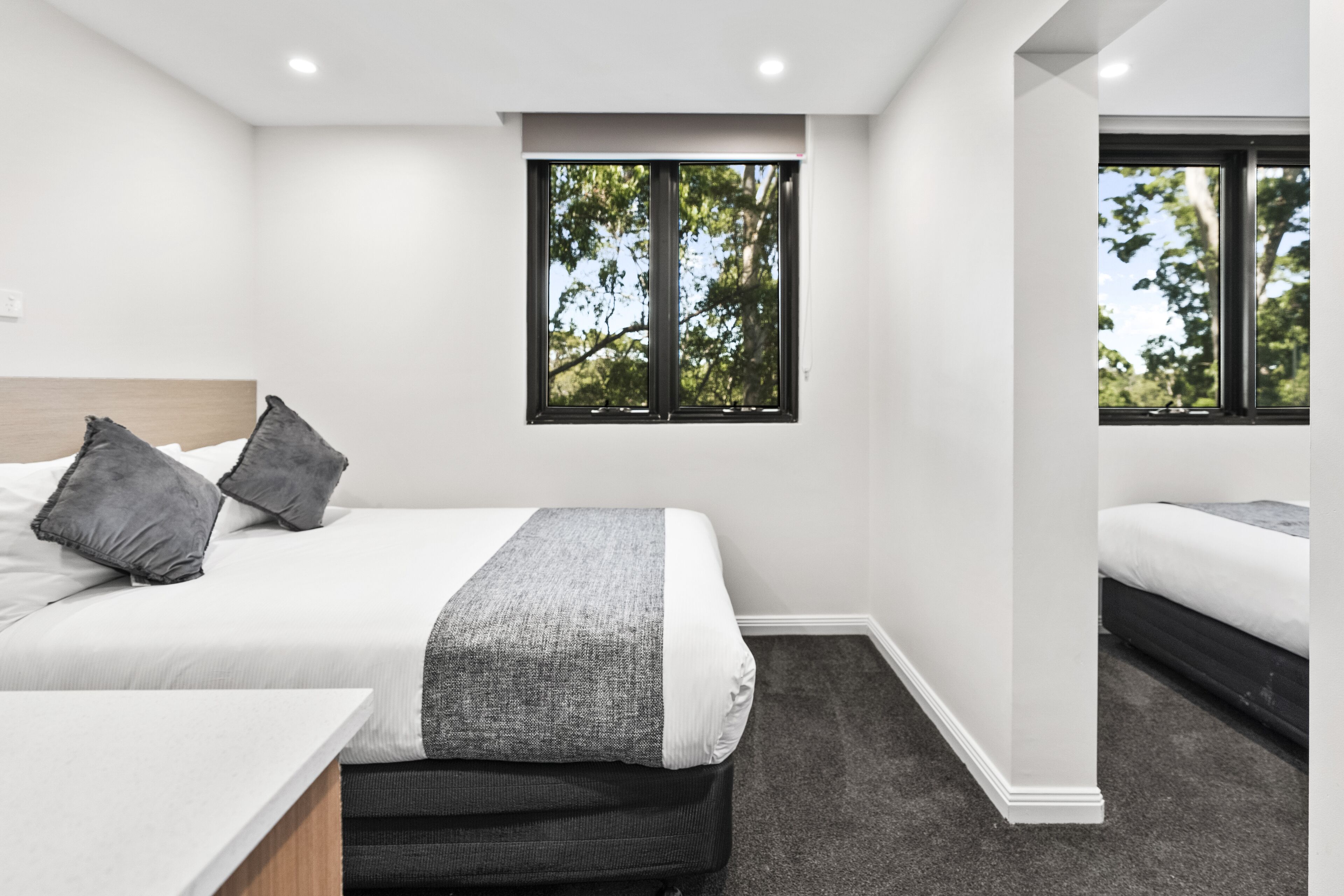 Un dormitorio moderno con una cama grande, un escritorio pequeño y una ventana con vistas a árboles.