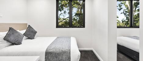 Un dormitorio moderno con una cama grande, un escritorio pequeño y una ventana con vistas a árboles.