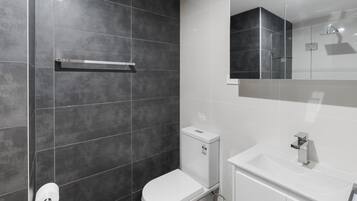 A modern bathroom with dark tiled walls, a white toilet, and a white sink with a mirror above it.