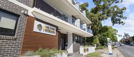 Un bâtiment moderne, avec une enseigne « Sutton & Co. » au rez-de-chaussée, caractérisé par une façade en briques et un décor de panneaux en bois.