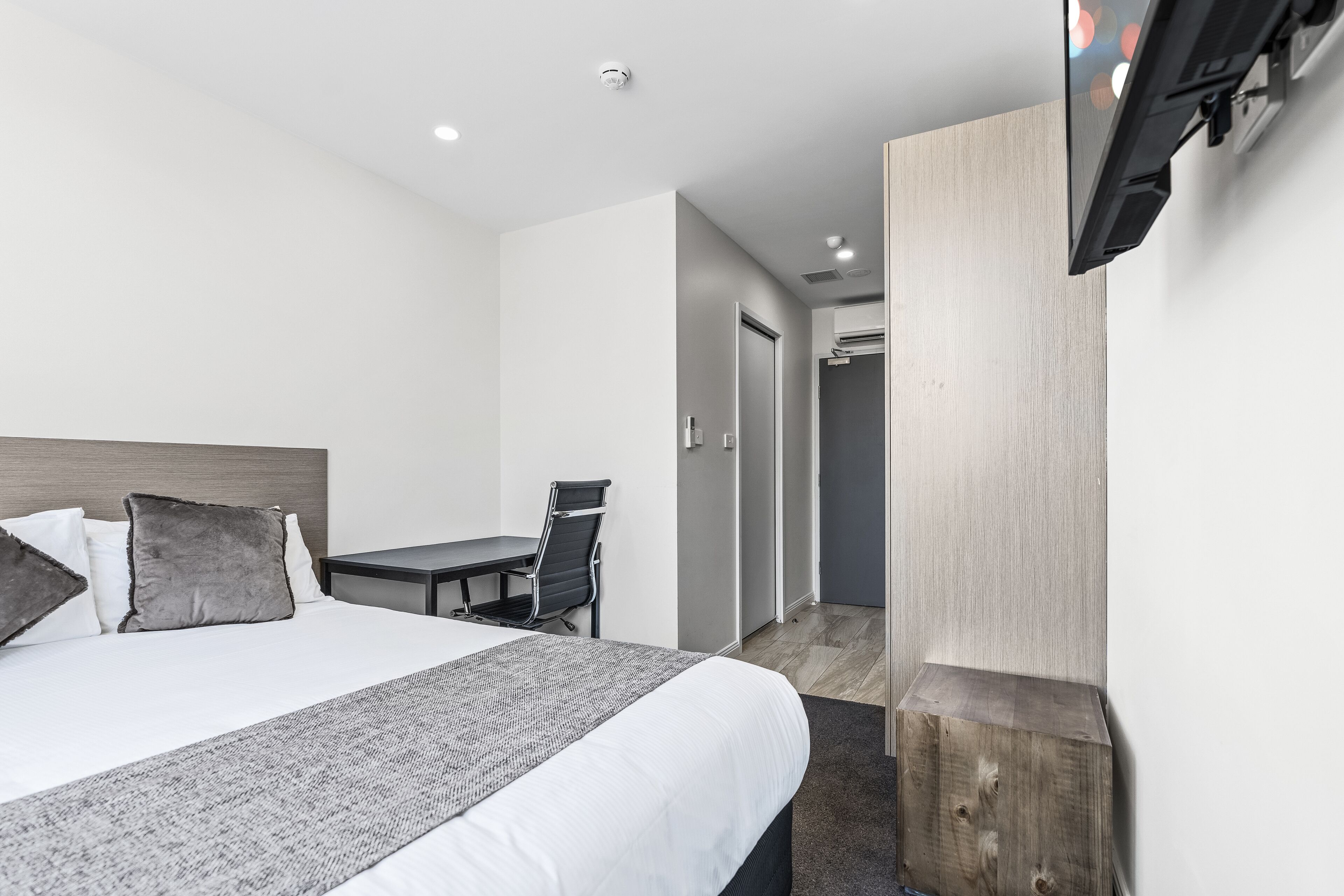 Una habitación de hotel moderna con una cama grande, un escritorio y un televisor de pantalla plana en la pared.