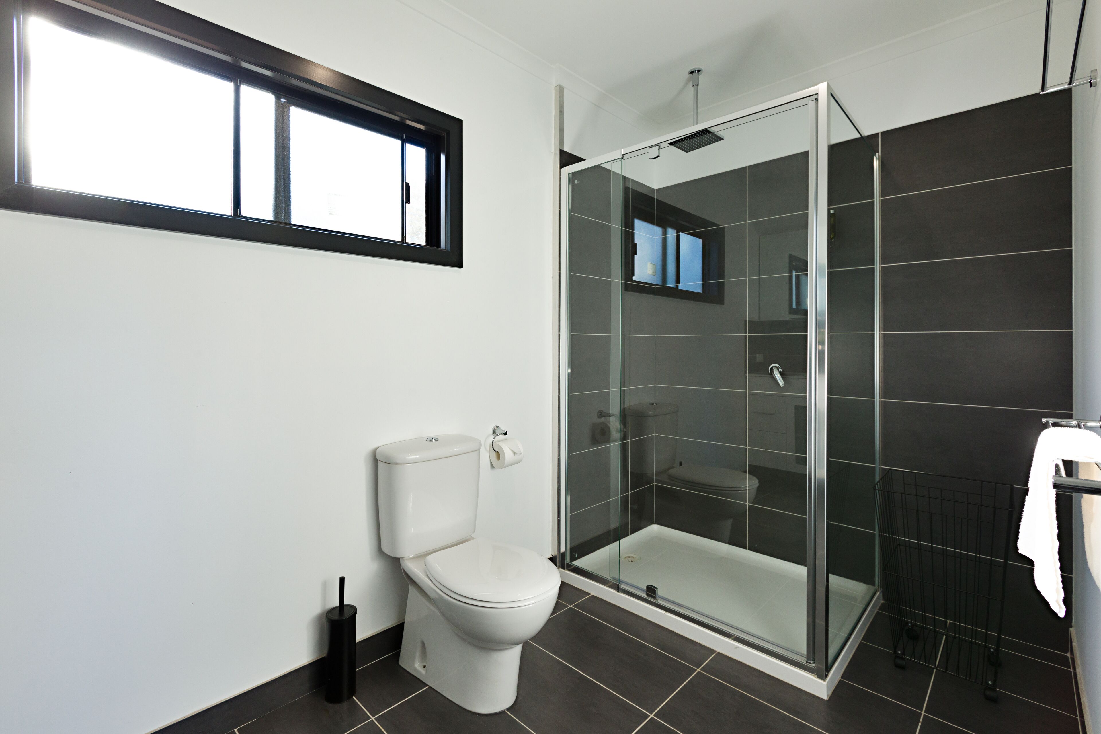 Un baño moderno con inodoro, ducha con cerramiento de vidrio y ventana sobre el inodoro.