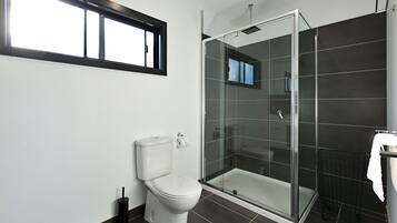 Un baño moderno con inodoro, ducha con cerramiento de vidrio y ventana sobre el inodoro.