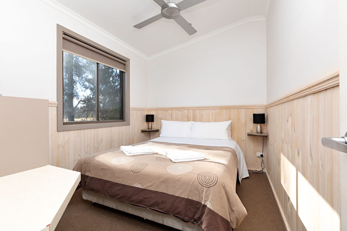 A bedroom with a bed, a window, a ceiling fan, and wooden paneling.