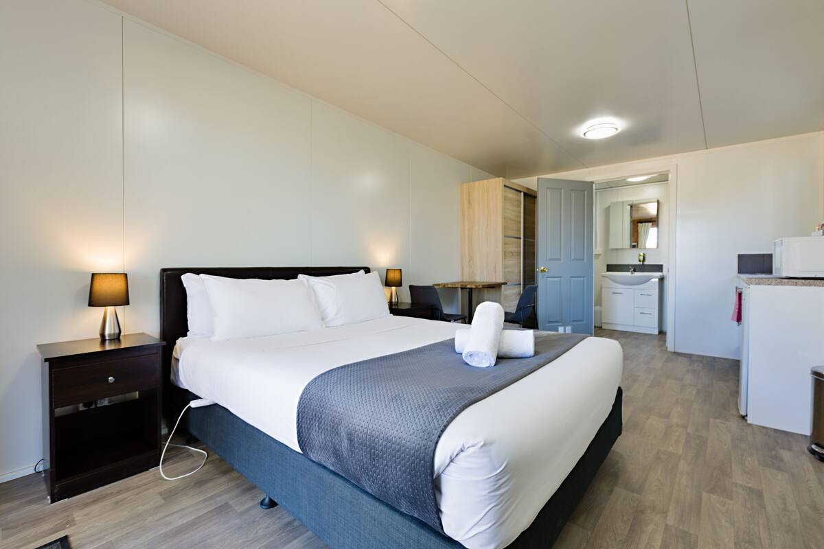 A modern hotel room with a neatly made bed, a small desk, and a bathroom visible through an open door.