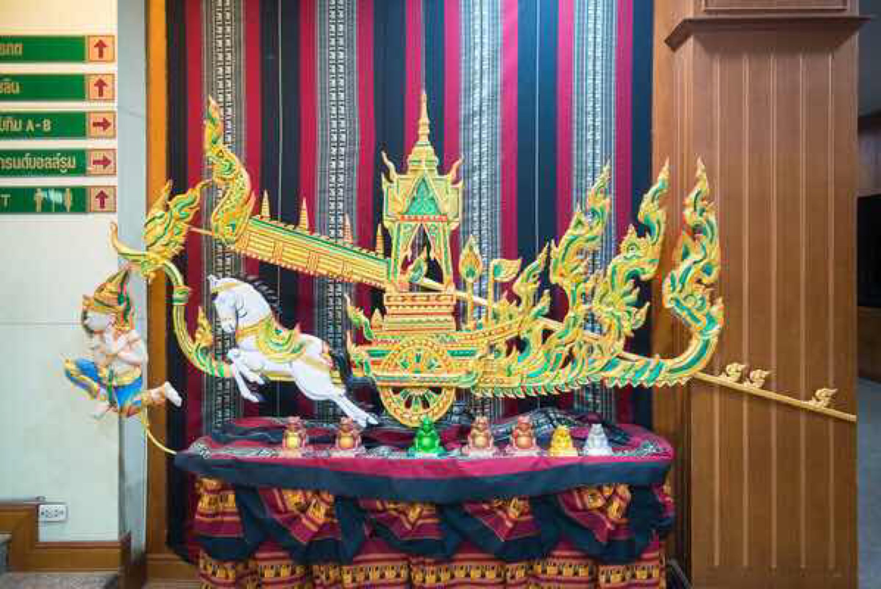 En traditionel thai-båd med detaljerede udskæringer og en figur på en hvid hest, placeret på et bord med et rødt klæde.
