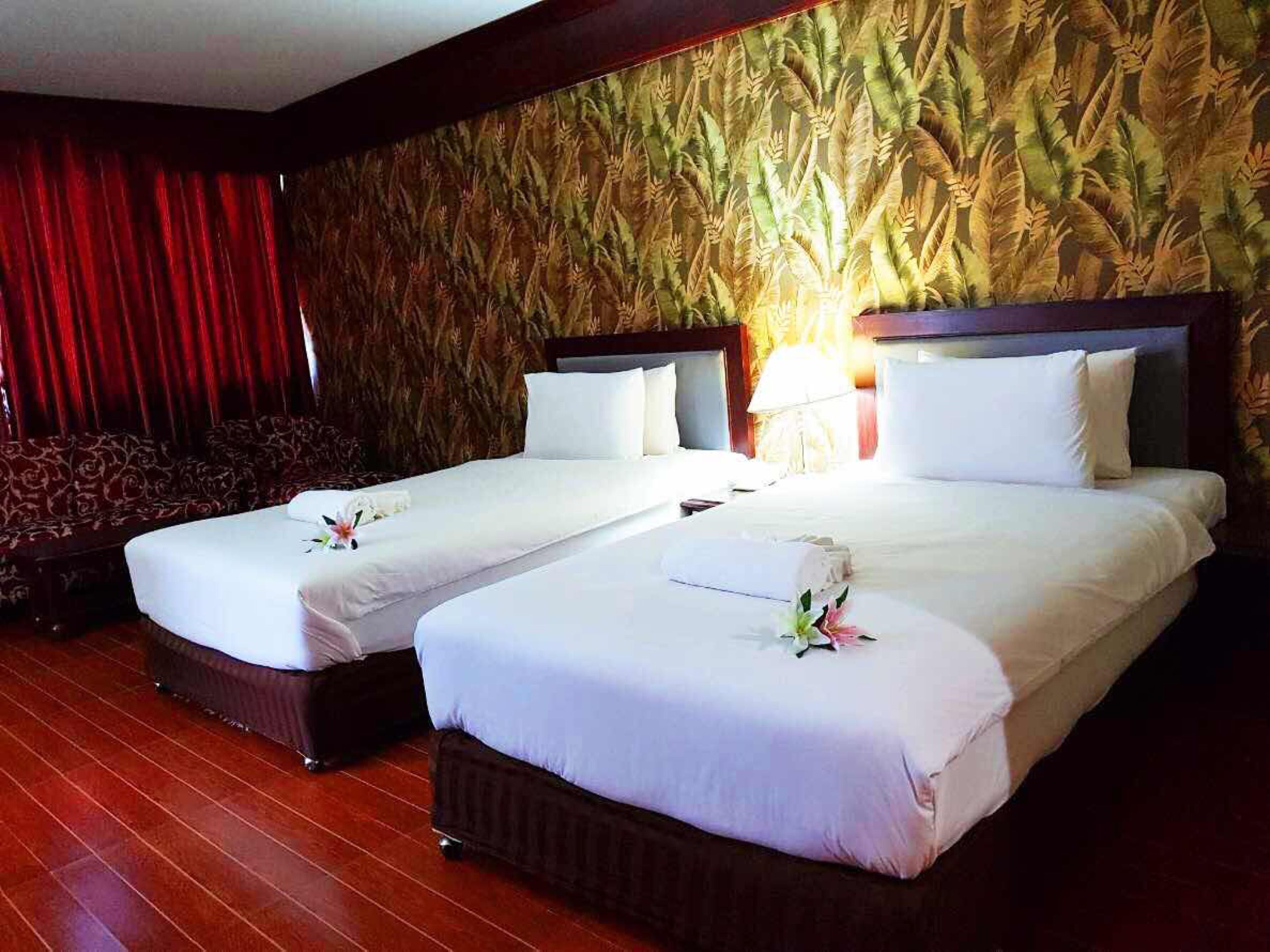 A hotel room with two beds, a red curtain, a patterned wall, and a wooden floor.