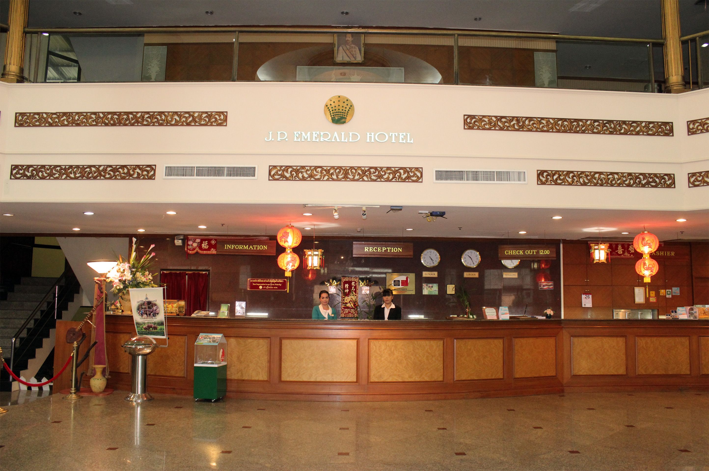 La recepción del Hotel J.P. Emerald, con un mostrador de salida, una mesa de recepción y una escalera que conduce a los pisos superiores.