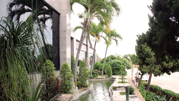 A serene courtyard with a water feature, lush greenery, and a modern building facade. - JP Emerald Hotel (Yasothon)