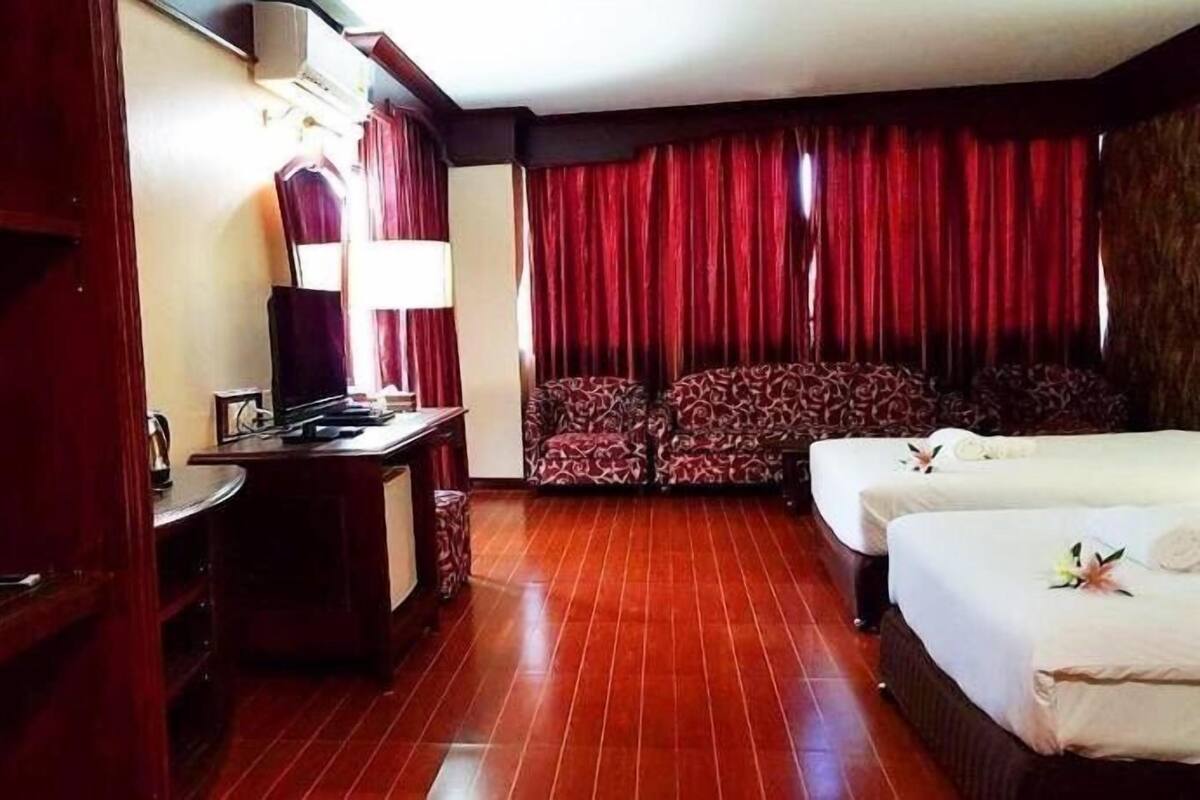 A hotel room with a desk, two chairs, a bed, and red curtains.
