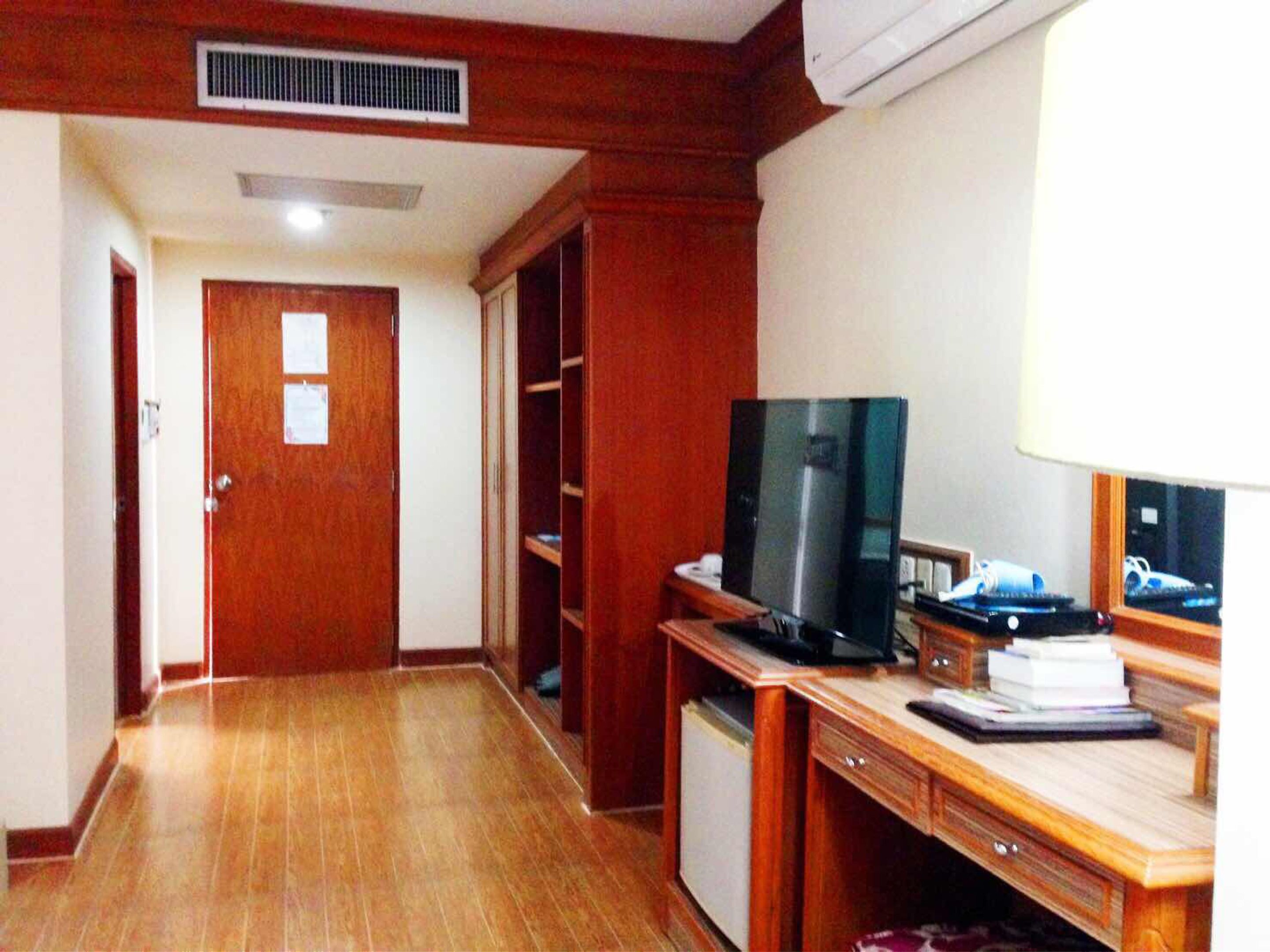 A hotel room with a wooden floor, a desk with a television, a mini-fridge, and a wardrobe.