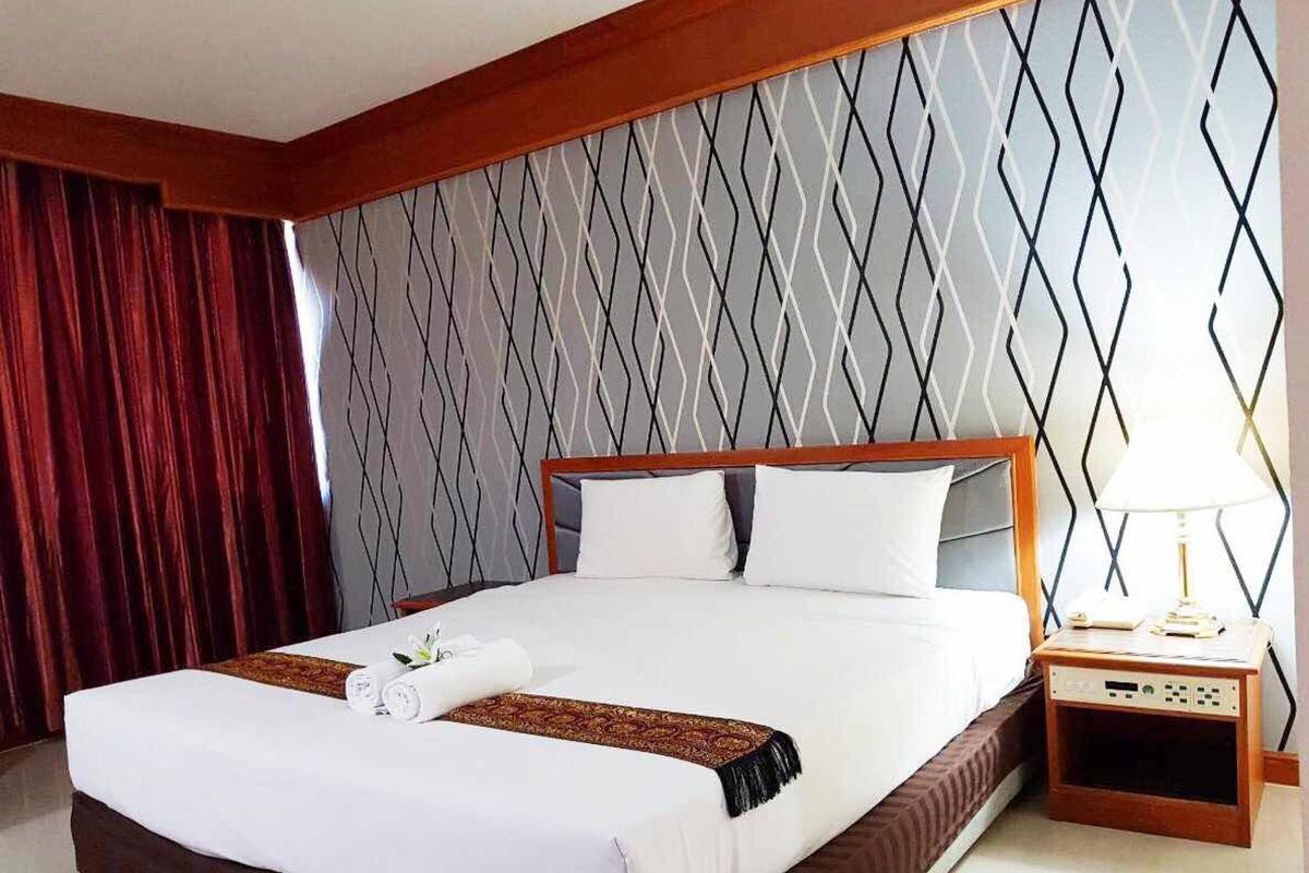 A hotel room with a large bed, a wooden headboard, a nightstand with a lamp, and a patterned wall.