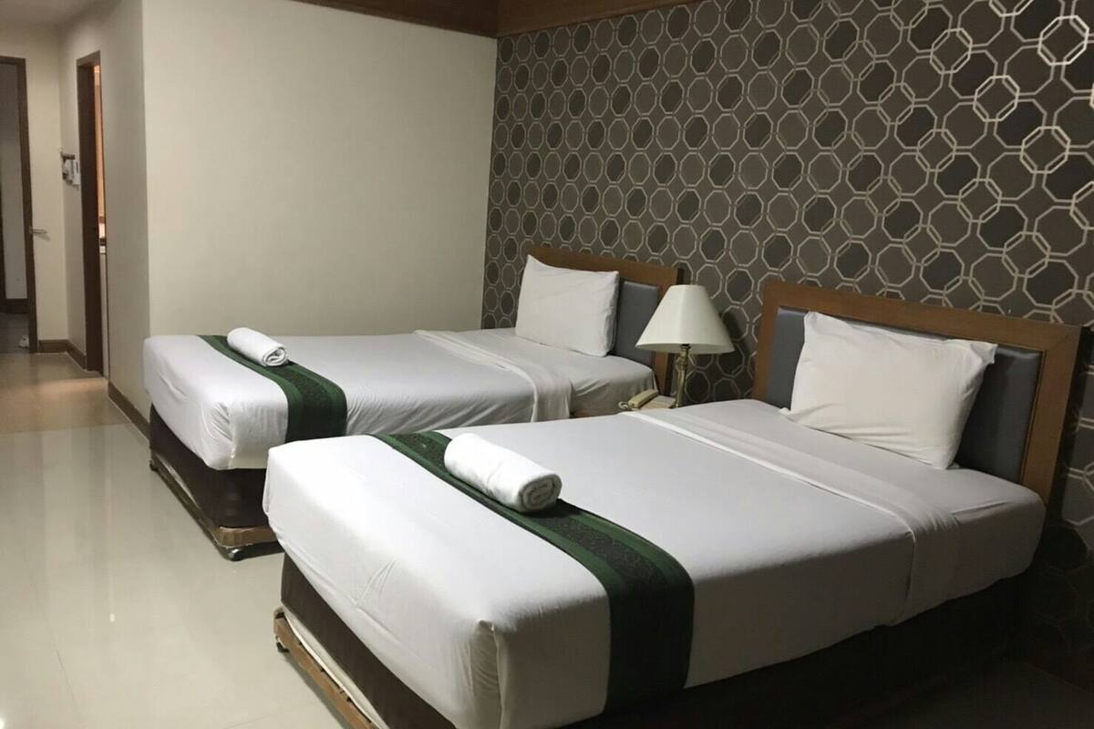 A hotel room with two beds, a patterned wall, and a bedside lamp.