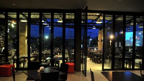 An indoor dining area with tables and chairs, large windows, and a view of the outside. - JP Emerald Hotel (Yasothon)