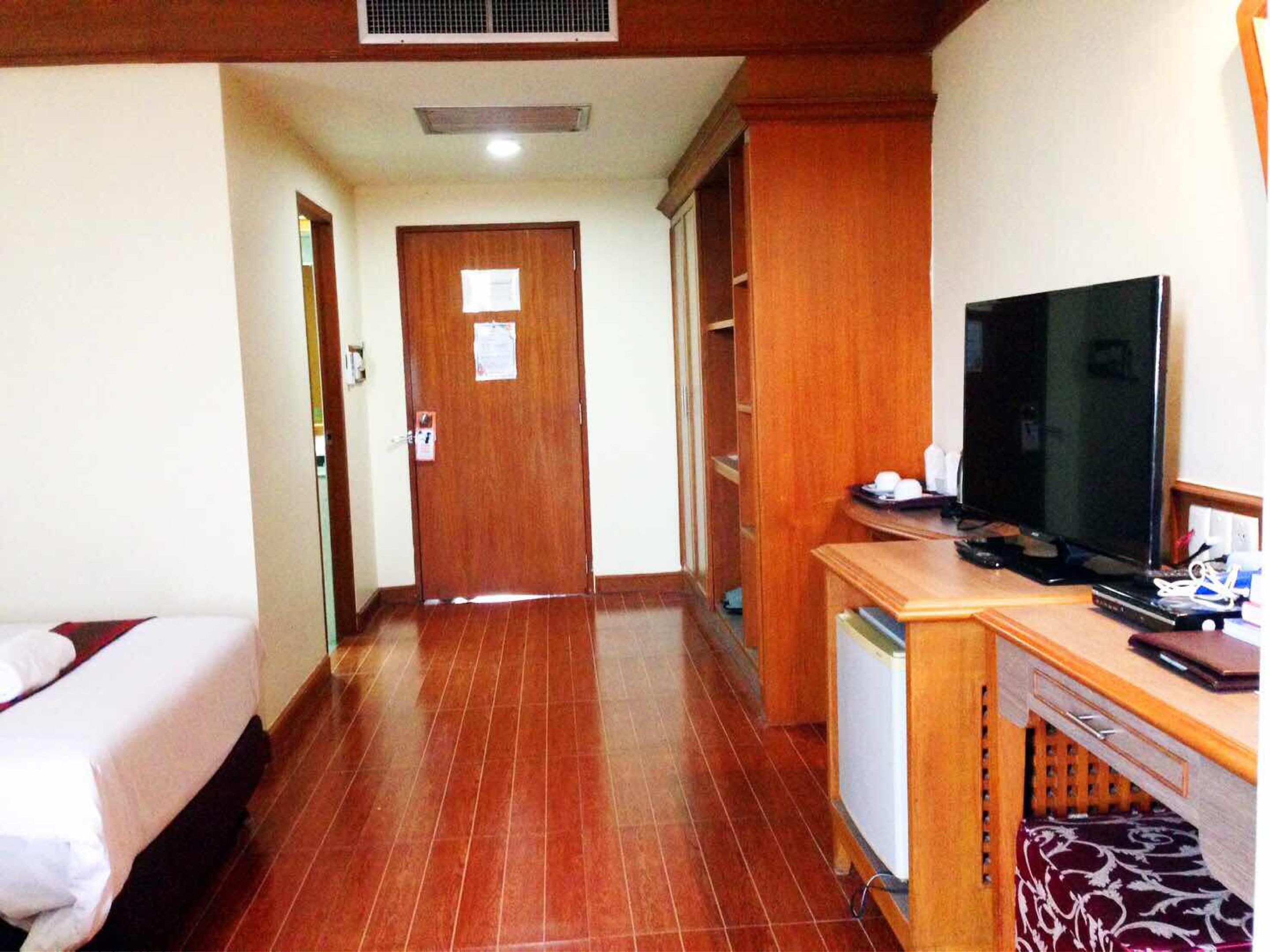 A hotel room with a bed, a desk with a television, and a door at the end of the hallway.