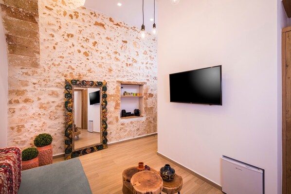 A modern room with a stone wall, a flat-screen TV, wooden furniture, and a small shelf with items.