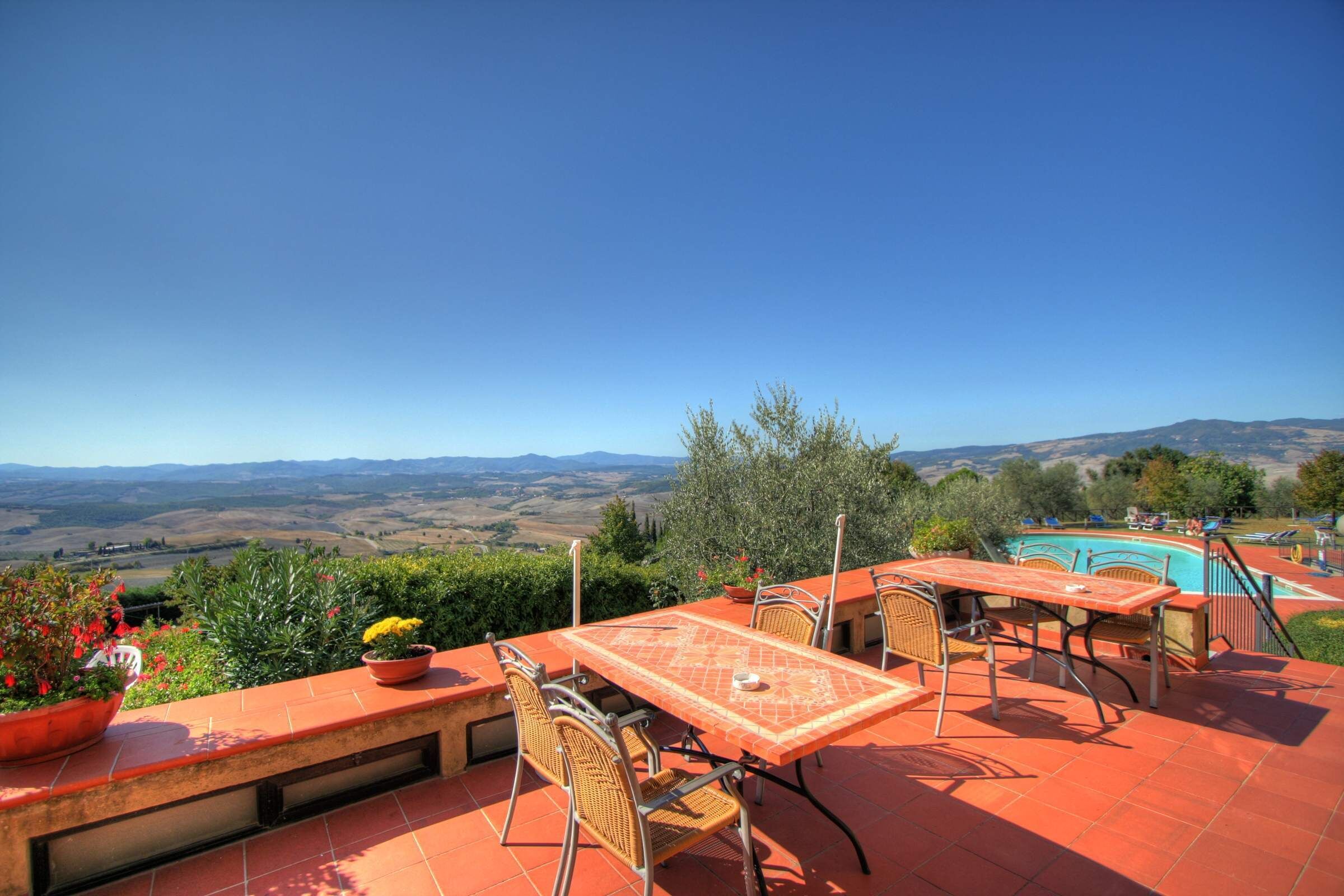 Eine Terrasse mit Tisch und Stühlen mit Blick auf einen Pool und eine hügelige Landschaft.