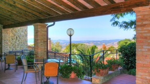 A covered patio with outdoor seating, stone walls, and a view of the landscape.