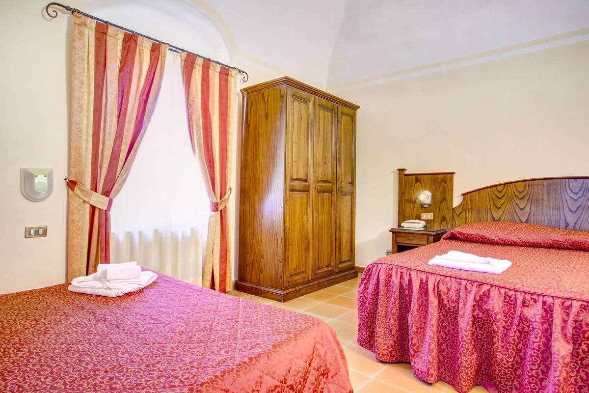 Une chambre d’hôtel avec deux lits, une armoire en bois, une table de chevet et un miroir dans la salle de bain.
