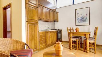 Une cuisine avec des meubles en bois, une table à manger avec des chaises, un fauteuil en osier et une table ronde sur laquelle est posé un pot en argile.