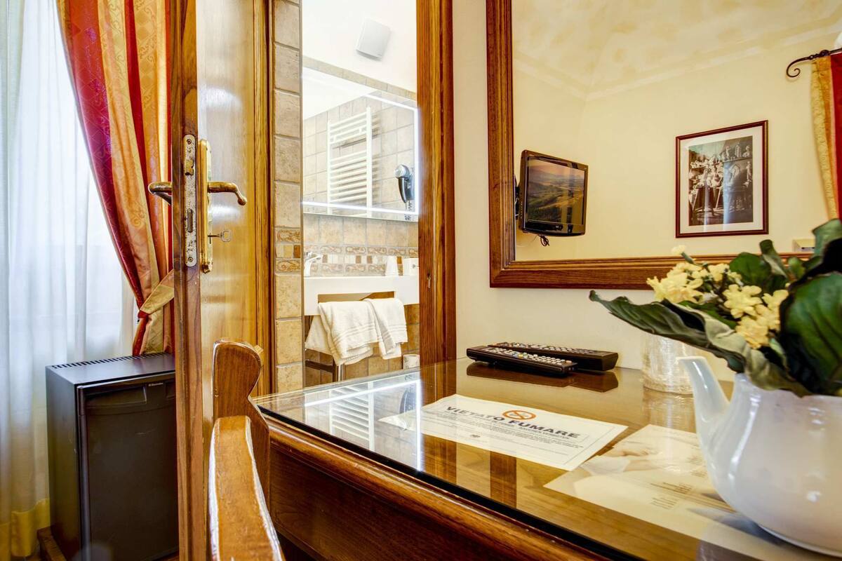 Un espace d’accueil d’hôtel avec un comptoir de réception en bois, un téléviseur, un vase de fleurs et un tableau encadré au mur.