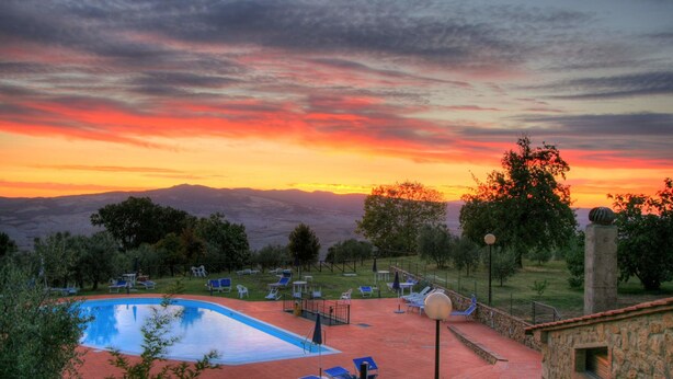 A swimming pool with lounge chairs and a stone building with a view of the mountains at sunset.