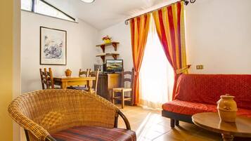 Una sala de estar con una silla de mimbre, un sofá rojo, una mesa de comedor con sillas, un televisor y una ventana con cortinas a rayas.