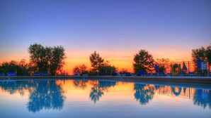 Uma área de piscina tranquila, com reflexos nítidos de árvores e céu ao pôr do sol.
