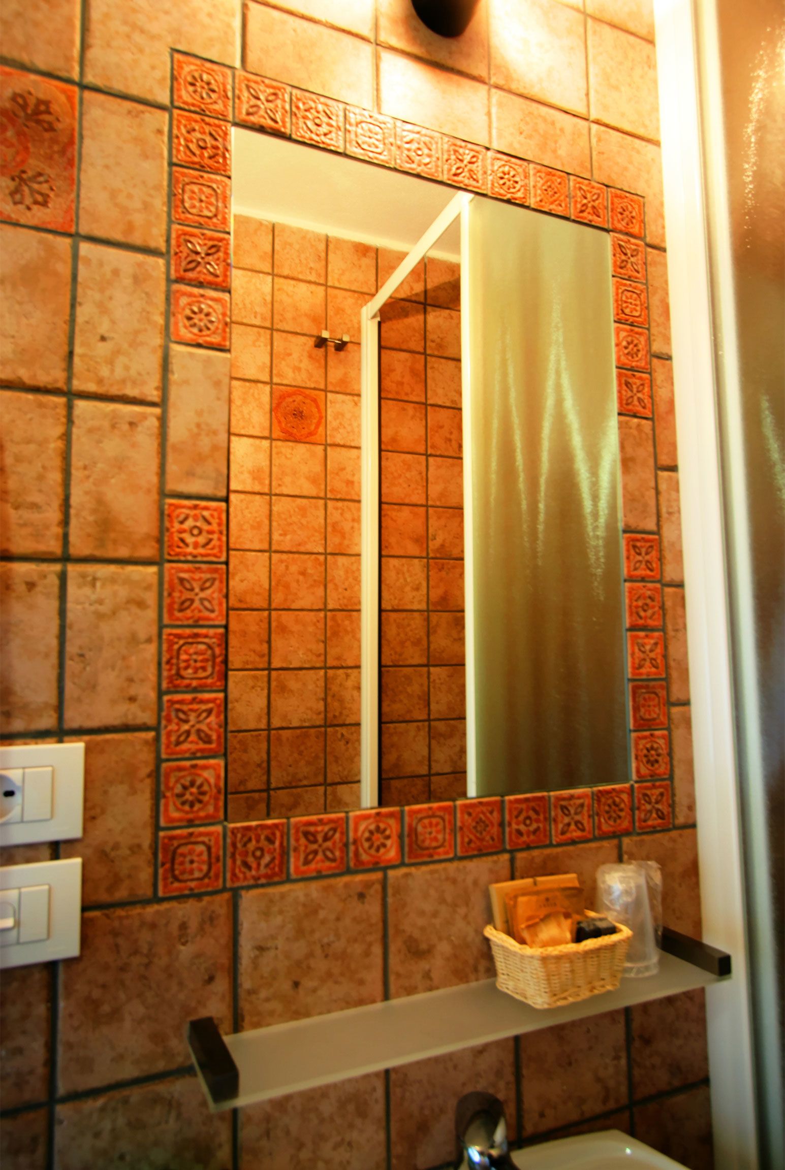 Un baño con pared de azulejos, un espejo, una repisa con una cesta y un perchero.