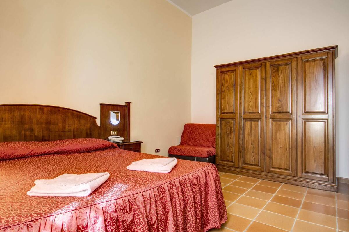 Une chambre d’hôtel avec un grand lit, une armoire en bois et un fauteuil rouge.