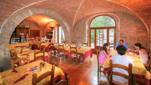 A restaurant with arched brick ceilings and wooden tables, featuring a stone wall and large windows.