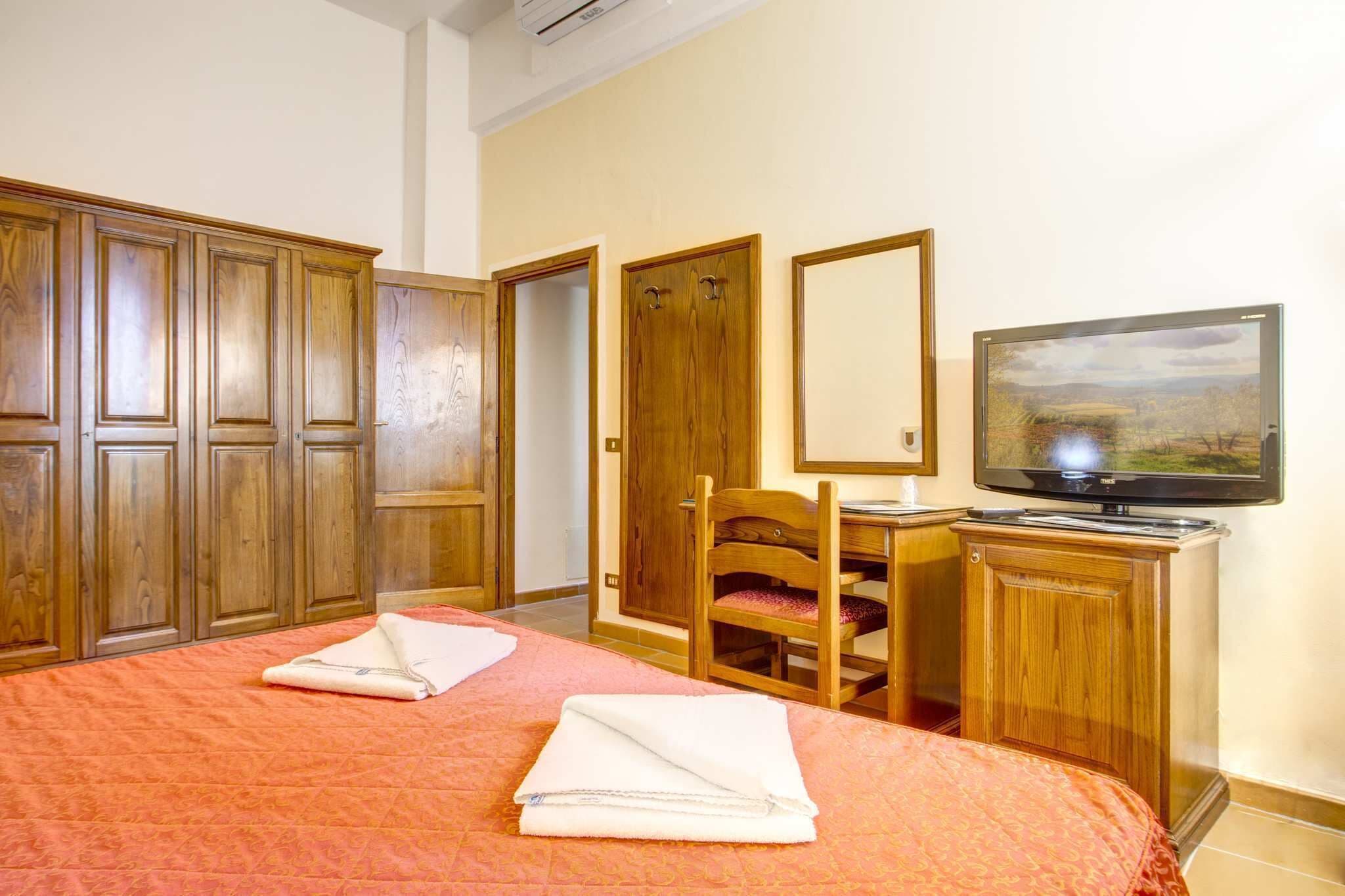 A hotel room with a bed, a desk with a chair, a television, and wooden wardrobes.