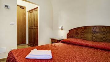 A hotel room with a bed, a wooden wardrobe, a nightstand, and a wall-mounted light fixture.