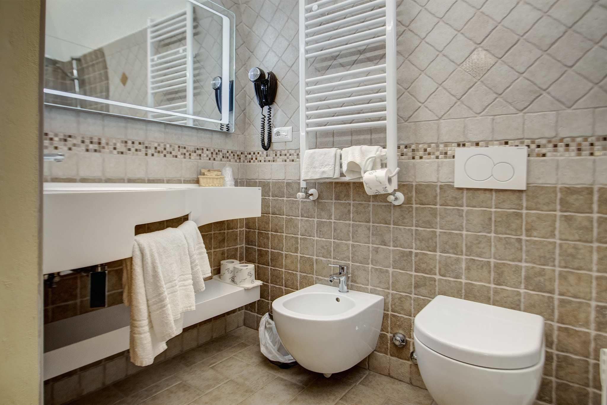 Un baño con bidé, inodoro, perchero para toallas y un secador de pelo montado en la pared.