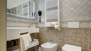 Un baño con bidé, inodoro, perchero para toallas y un secador de pelo montado en la pared.
