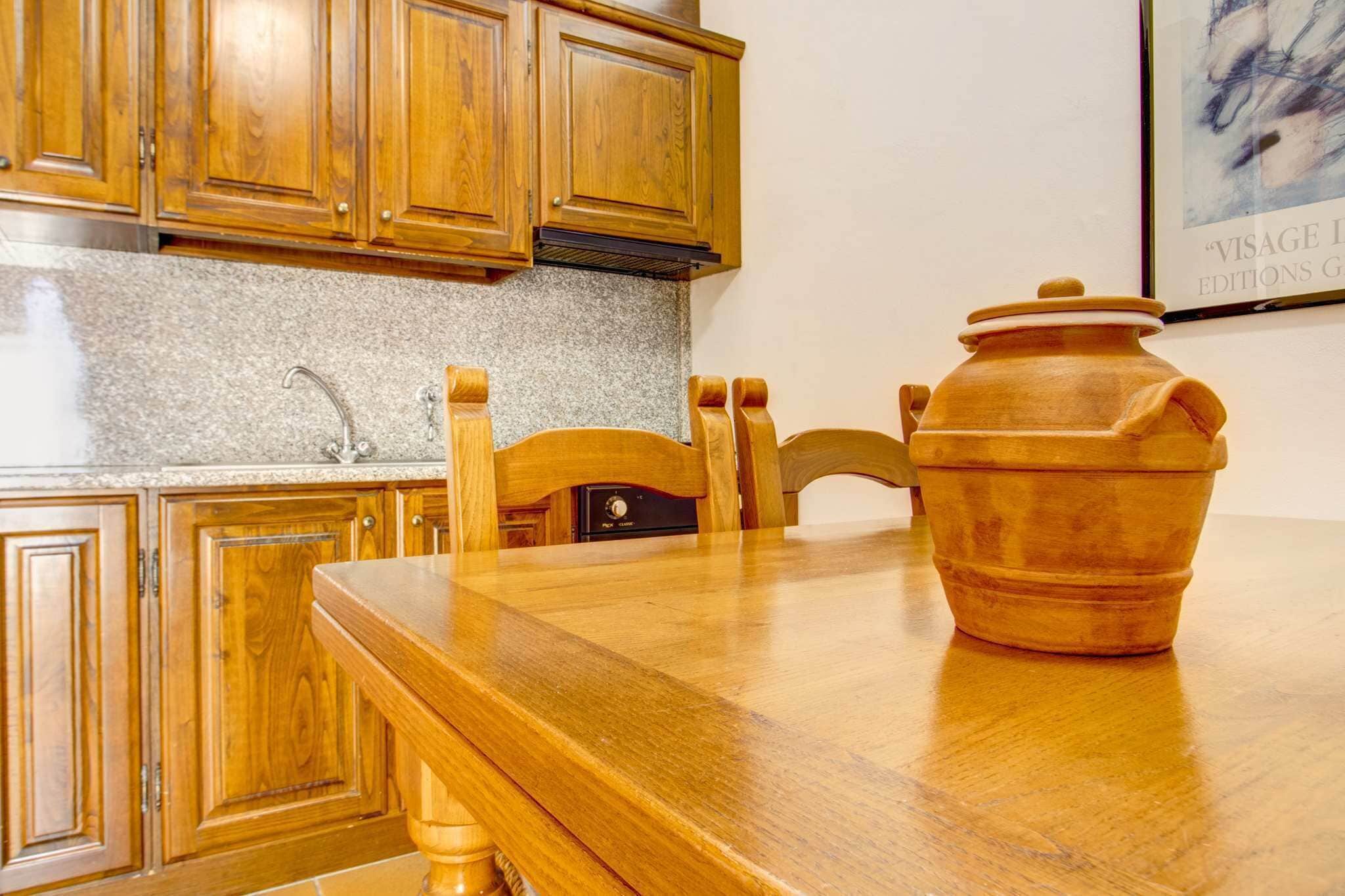 A kitchen with wooden cabinets, a granite countertop, and a large clay pot on the table.