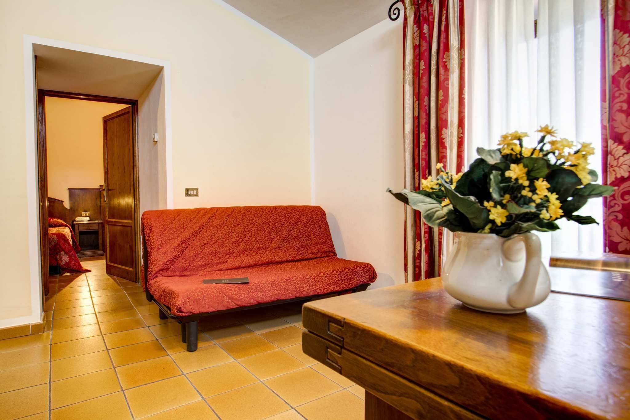 Una stanza con un divano, un tavolo in legno con un vaso di fiori, una porta che dà su un'altra stanza e una finestra con tende.