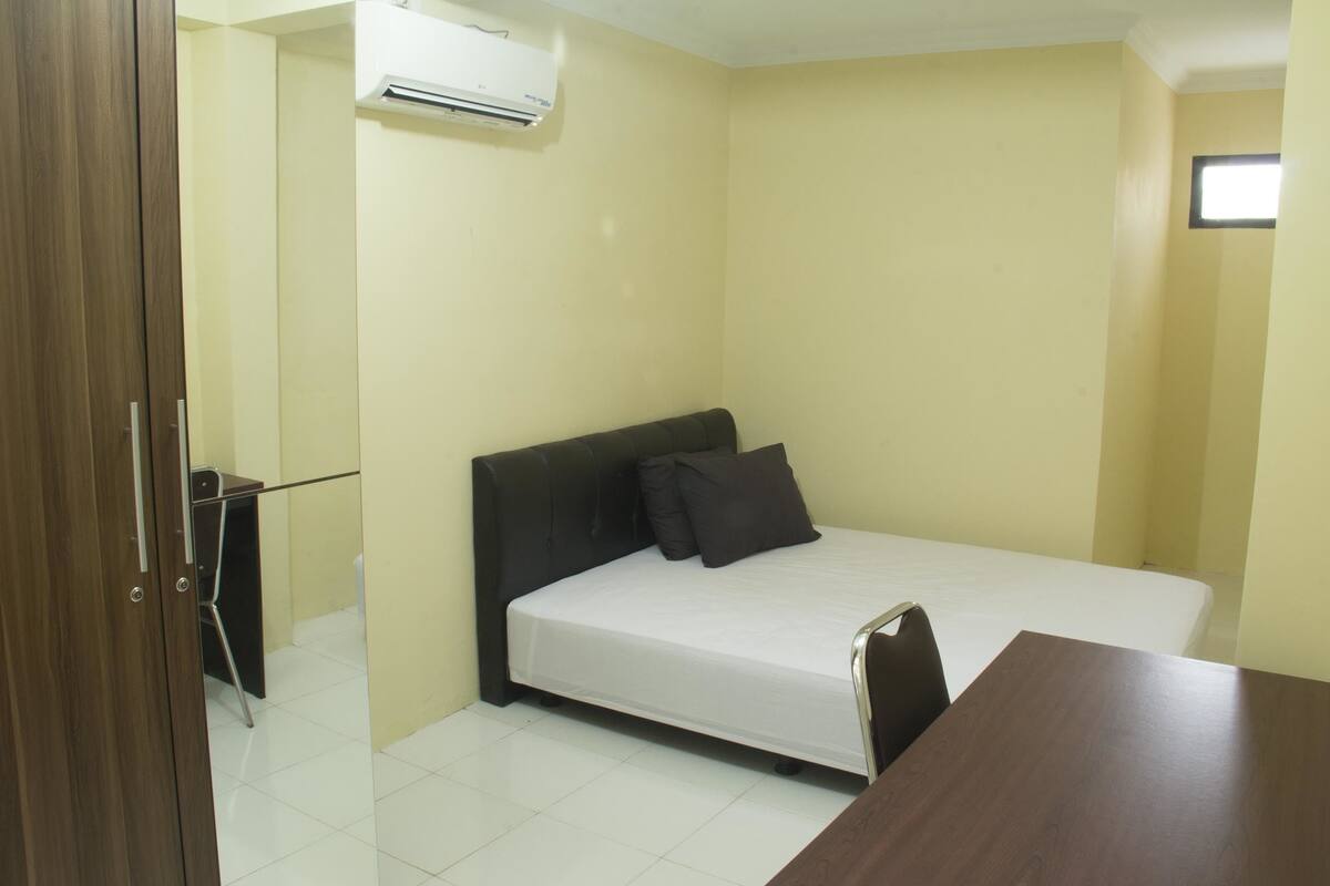 A small, single-bed room with a wooden headboard, a bedside table, and a chair.