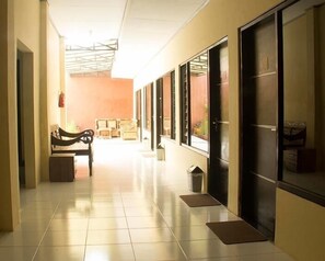 Um corredor com um banco, um cesto de lixo e uma porta com janela.
