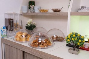 En morgenmadsbuffet med overdækkede madvarer og en lille potteplante.