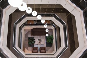 En rummelig lobby med et centralt siddeområde, en trappe og en moderne lysekrone.