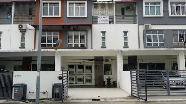 A multi-story residential building with a gated entrance, a satellite dish, and a sign advertising a homestay service.