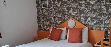 A single bed with a white mattress and pillows, an orange headboard, and a floral-patterned wallpaper.