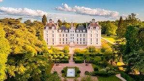 Un edificio grande y simétrico con un patio central, rodeado de jardines cuidados y árboles.